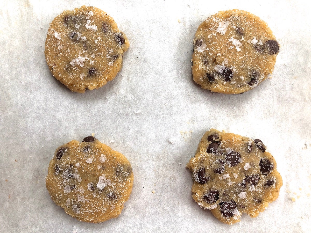 Dough for Gluten-Free Almond Flour Chocolate Chip Cookies scooped onto a baking sheet, flattened, and sprinkled with flaked sea salt before baking.